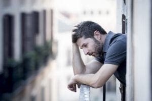 Depression - Man leaning on balcony railing holding hand on head depressed thinking.